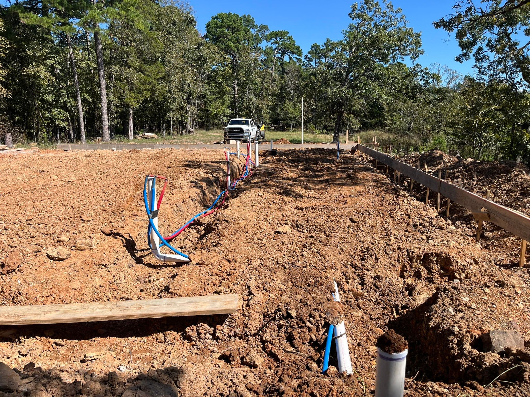 Construction site showing a foundation with plumbing lines and a pickup truck in the background.