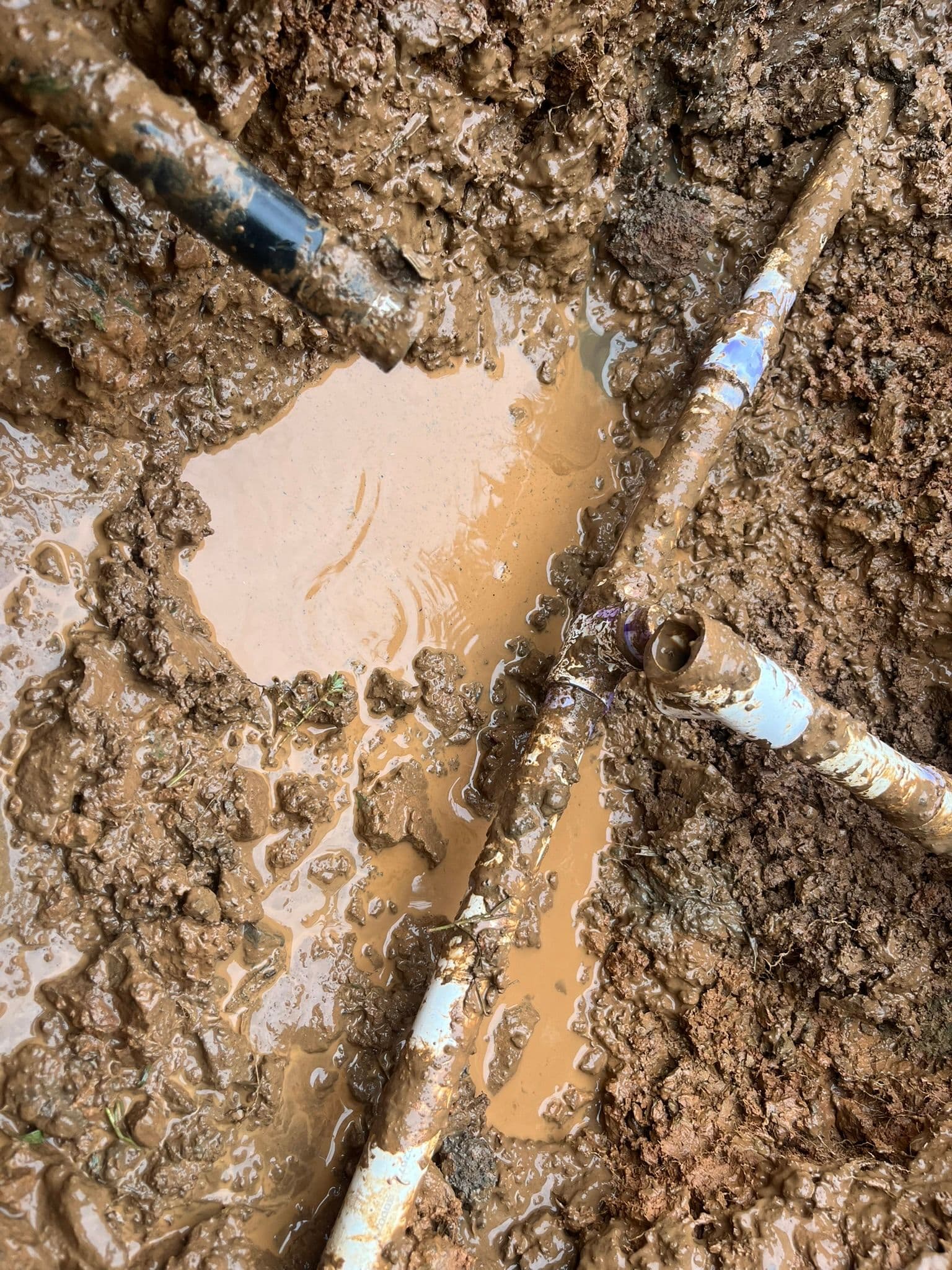Mud-filled excavation site with exposed pipes and water accumulation.