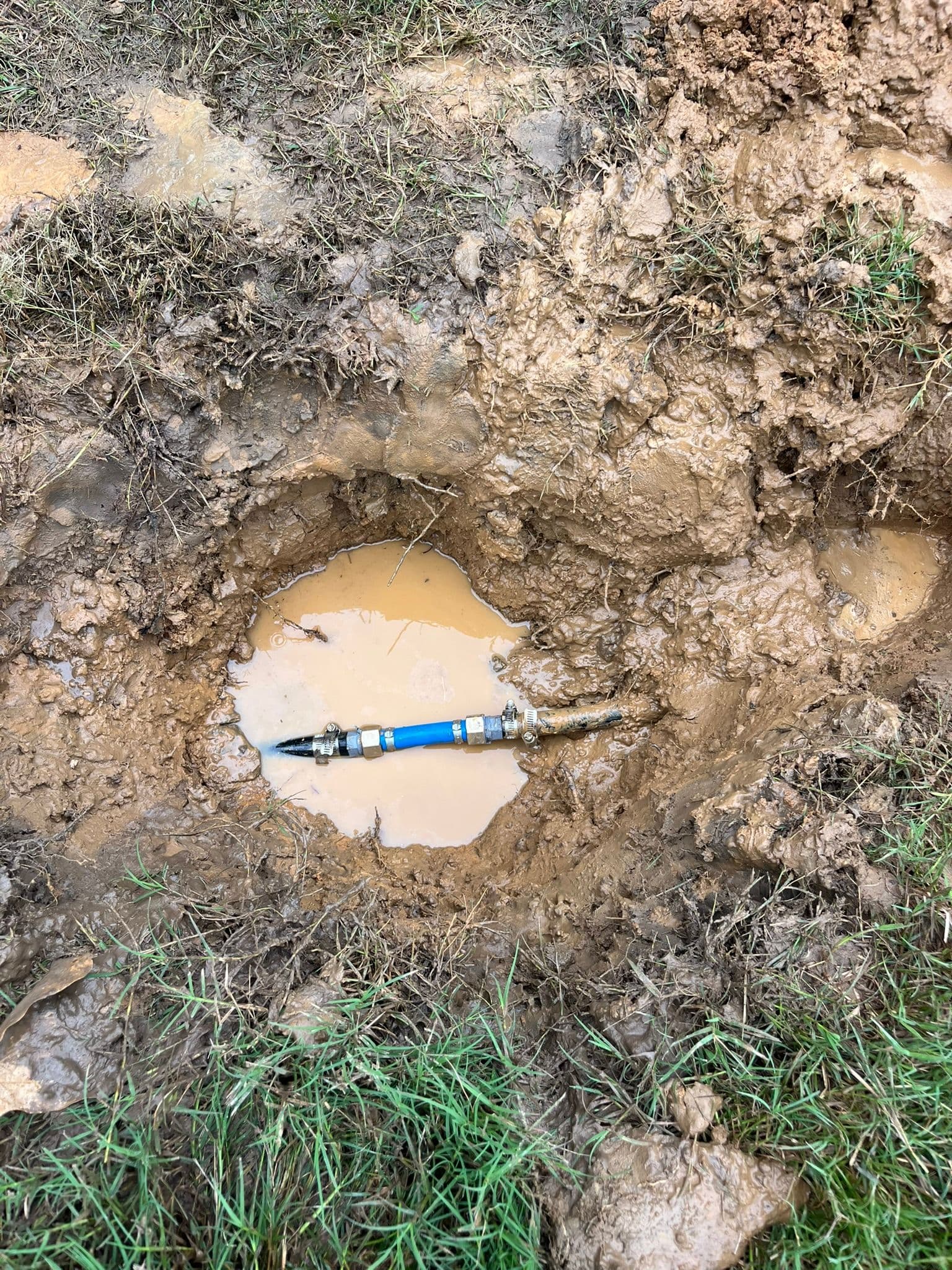 Water leak repair site showing a valve in muddy ground with pooling water.